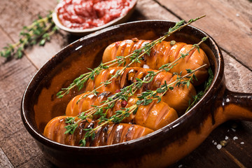 Sausages with thyme in a ceramic pan on wooden background.