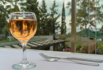 A glass of rose wine is a close-up on a white tablecloth on a table outdoors, in the background is nature. Trees are wonderfully reflected in the glass