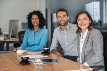 Smiling businesspeople sitting together at an office table - obrazy, fototapety, plakaty
