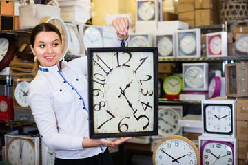 Woman is choosing new clock for her home in the store.