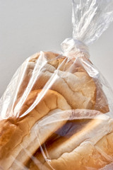 Three buns in a plastic bag. Bread packed in transparent plastic on light background with copy space. Zero waste shopping, plastic free, stop pollution, ecological concept.  