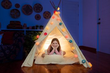 Attractive cute girl sitting inside tepee tent in her bedroom enjoy happy time.