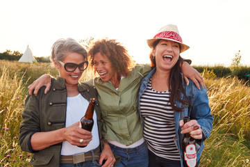 Group Of Mature Female Friends Walking Through Field On Camping Vacation Drinking Beer