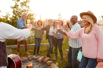 Group Of Mature Friends Sitting Around Fire And Making A Toast At Outdoor Campsite Bar