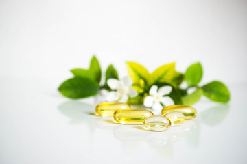 Close up soft capsules with leaves and white flora on white background with copy space for text.