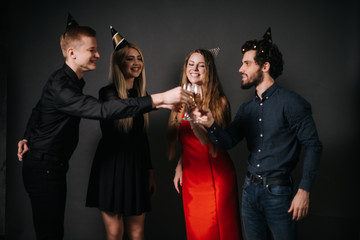 Four beautiful and cheerful friends are clinking glasses with champagne. Shooting in professional studio on isolated black background.