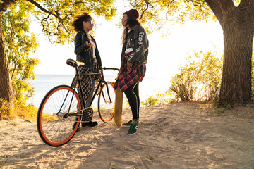 Two young attractive african girlfriends at the forest with bicycle