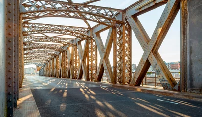 Foto op Canvas Asfaltweg onder de staalconstructie van een brug in de stad op een zonnige dag. Avond stedelijke scène met de zonnestraal in de tunnel. Stadsleven, vervoer en verkeer concept. © sergiymolchenko