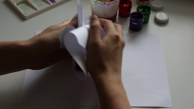 Hands crumpled a sheet of paper with paint. 