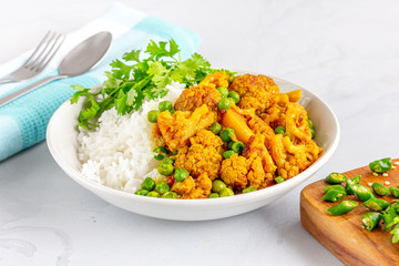 Aloo Gobi, Rice and Cauliflower Curry with Green Peas in a Bowl Garnished with Cilantro Top View Photo on White Background.