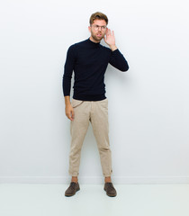 young full body man looking serious and curious, listening, trying to hear a secret conversation or...