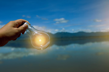 hand holding light bulb against nature, icons energy sources for renewable