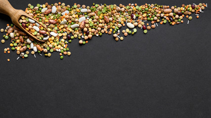 Colorful mixed legumes and cereals with wooden scoope on black background.