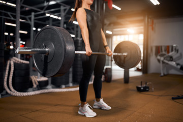 Fototapeta na wymiar Young unrecognizable woman with heavy barbell in hands, doing squats, preparing for powerlifting competition, spending time in modern gym, active people concept, side sho