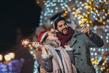 Obraz premium Young loving couple burning sparklers by holiday illumination on new years eve.