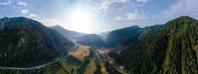Fototapeta premium Wide aerial view of a camping site, recreation with a tent and parking for a motor home, camper van, sunrise summer, mountains and a river near the town of Predazzo, Trentino, Italy, Europe