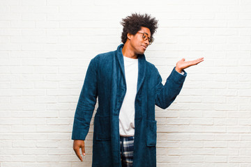 young black man wearing pajamas with gown feeling happy and smiling casually, looking to an object...