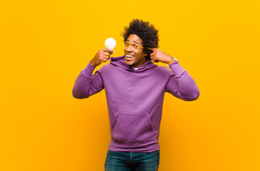 young african american man with a light bulb against orange back