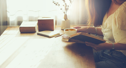 Young female reading old book and drink cofee after work with sunlight through the window in the...