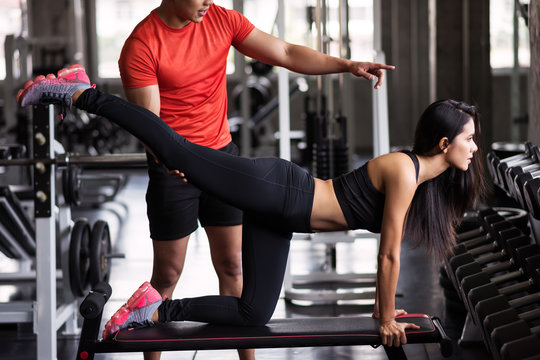 Trainer coach stretching leg to girl in gym