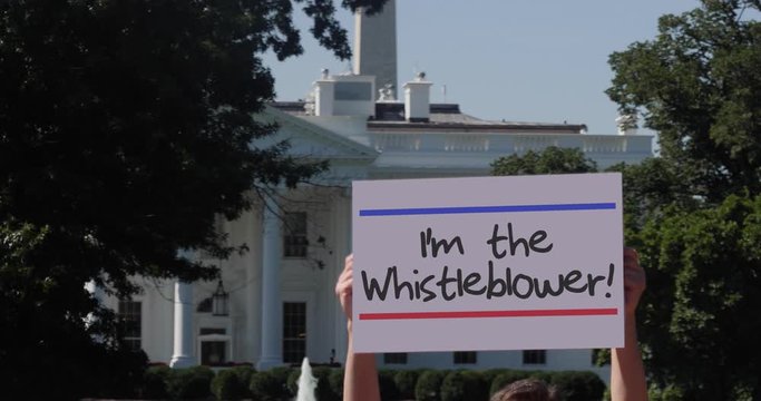 A man holds a I'm the Whistleblower protest sign outside the White House.	
