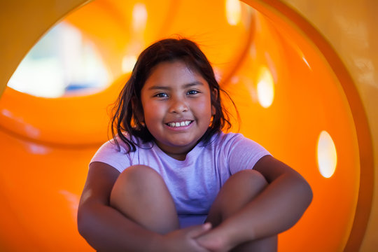 A nine year old girl having fun playing in a yellow playground slide.