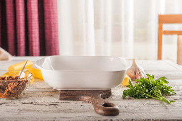 White baking dish and pasta with vegetables. White dish in the center of the table with products....