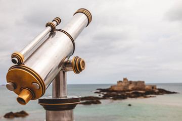 Tourist monocular telescope on the terrace of Saint Malo opposite the Fort National fortress - obrazy, fototapety, plakaty
