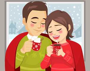 Cute couple on Christmas winter time enjoying hot drink mug under red blanket