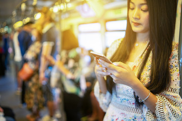 digital travel concept. young Asian woman traveling by the train or Mass Rapid Transit(MRT) train near the window using smartphone in a subway, she texting message and Watching Movie On Mobile Phone