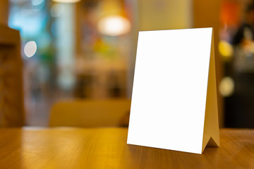 Mock up Label the blank menu frame in Bar restaurant ,Stand for booklets with white sheets paper acrylic tent card on wooden table cafeteria blurred background can inserting the text of the customer.