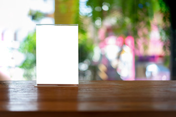 Mock up Label the blank menu frame in Bar restaurant ,Stand for booklets with white sheets paper acrylic tent card on wooden table cafeteria blurred background can inserting the text of the customer.