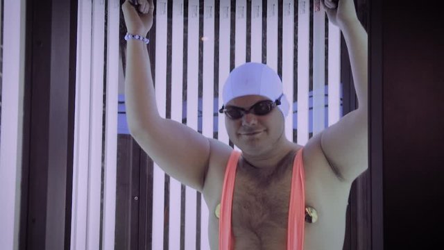 Full man sunbathes in tanning beds and dances.