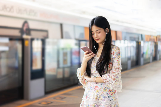 digital travel concept. young Asian woman traveling by the train or Mass Rapid Transit(MRT) train near the window using smartphone in a subway, she texting message and Watching Movie On Mobile Phone