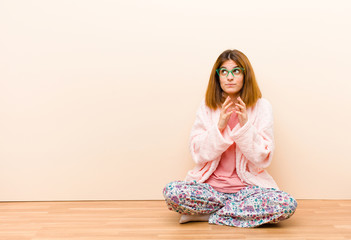 young woman wearing pajamas sitting at home scheming and conspiring, thinking devious tricks and...