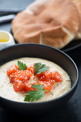Close-up of hummus with salmon fillet, parsley and sesame seeds served in a black bowl, vertical shot
