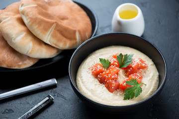Bowl of hummus with salmon, sesame, parsley and pita bread, studio shot over black stone background