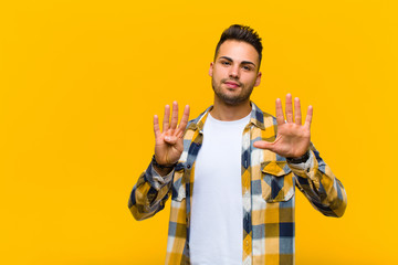 young hispanic man smiling and looking friendly, showing number nine or ninth with hand forward,...