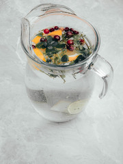 Lemonade pitcher with lemon slices, mint leaves, red berries and ice on glass jug. View with copy space