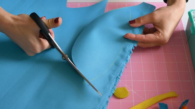 A professional seamstress cuts out the details of clothes from the fabric with scissors