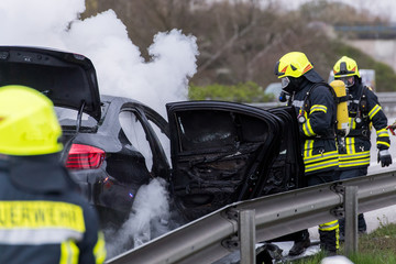 Feuerwehrmänner löschen ein brennendes Auto