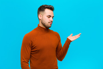 young hispanic man feeling happy and smiling casually, looking to an object or concept held on the...