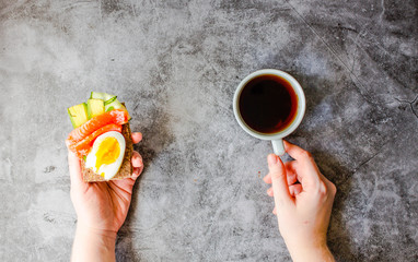 Buckwheat gluten-free bread with avocado and fresh salted salmon fillet with eggs on a gray marble background. Top view. Space for text. Close-up of male hands with food rich in fat and protein