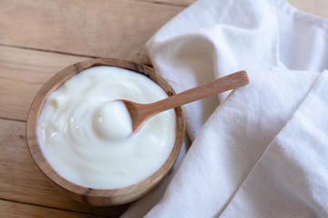 Natural homemade plain organic yogurt in wooden bowl and wood spoon on wood texture background