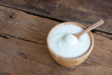 Natural homemade plain organic yogurt in wooden bowl and wood spoon on wood texture background