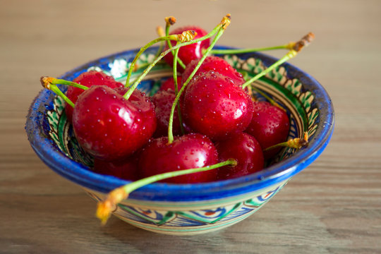 A beautiful bowl with Uzbek national patterns filled with juicy fresh cherries