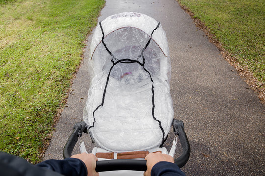 Father hands pushing white baby stroller with transparent cover. Outside walking in rainy day. Point of view shot.