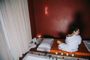 Fototapeta na wymiar attractive woman in bathrobe sitting on massage mat in spa salon