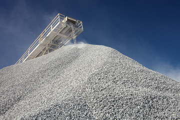 Conveyor line transporting crushed ore and pile of gravel against the blue sky, close-up. Mining industry. Mine and quarry equipment.
