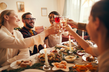 Side view portrait of elegant young people clinking champagne glasses while enjoying Christmas dinner at home